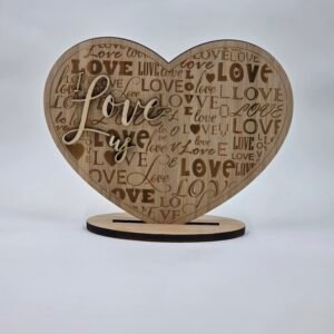 Freestanding wooden heart card engraved with an all-over “LOVE” pattern and raised script reading “I Love Us,” displayed on a stand.