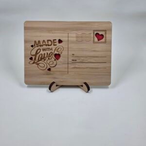 Wooden postcard keepsake engraved “Made With Love” with stamp and postmark details and heart cutouts, displayed on a small stand.