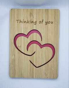Wooden “Thinking of you” card with layered heart cutout design and pink accent backing, shown on a white background.